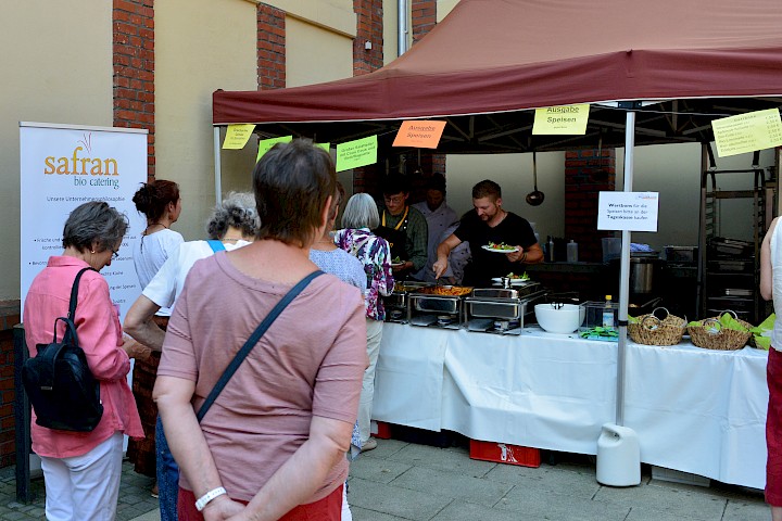 Einige Menschen stehen am Catering-Stand der Weltladen-Fachtage 2019 an. Dort wird das Mittagessen ausgegeben.