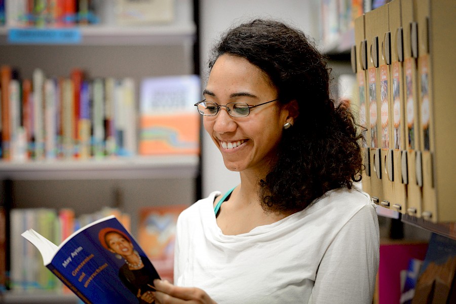 Junge Frau bei der Bildungsarbeit im Weltläden. Bildungsreferentin liest Buch vor Bildungssäule.